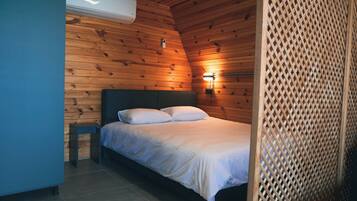 A bedroom with a wooden ceiling, a bed with white bedding, a nightstand, and a wall-mounted light fixture.