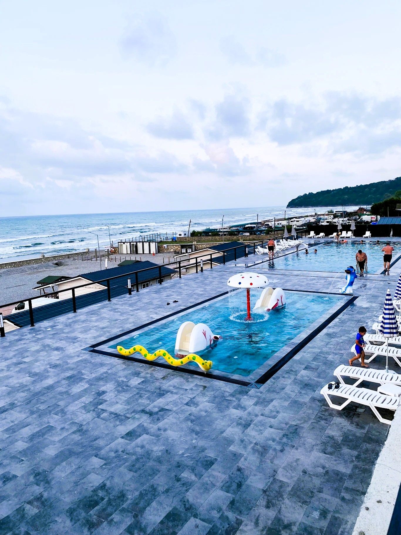 Area piscina con vista sul mare, una postazione di salvataggio e lettini.