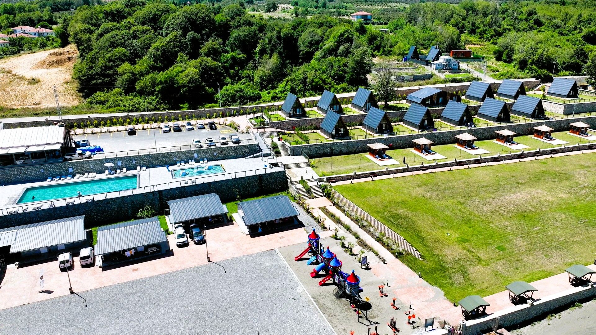 An aerial view of a resort with a swimming pool, multiple lodging units, and a grassy area.