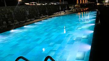 A swimming pool with clear blue water, surrounded by a stone wall and equipped with lounge chairs and umbrellas.