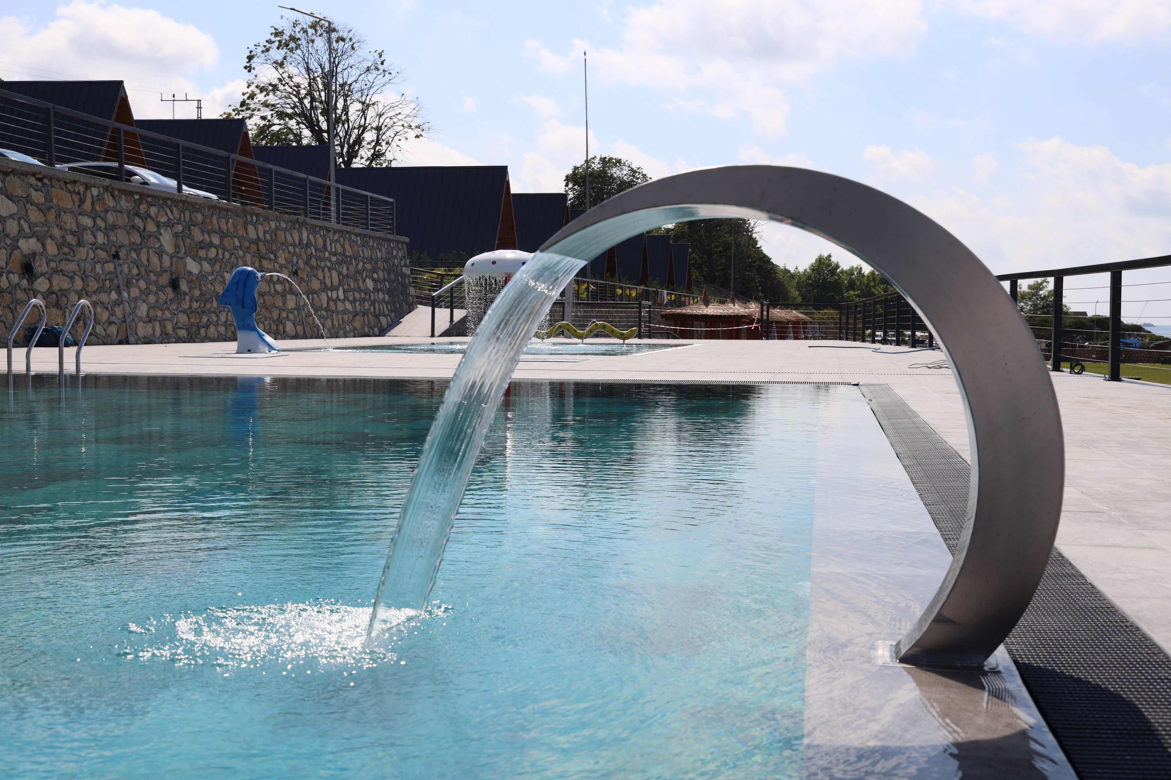 A swimming pool with a water feature and a stone wall in the background.