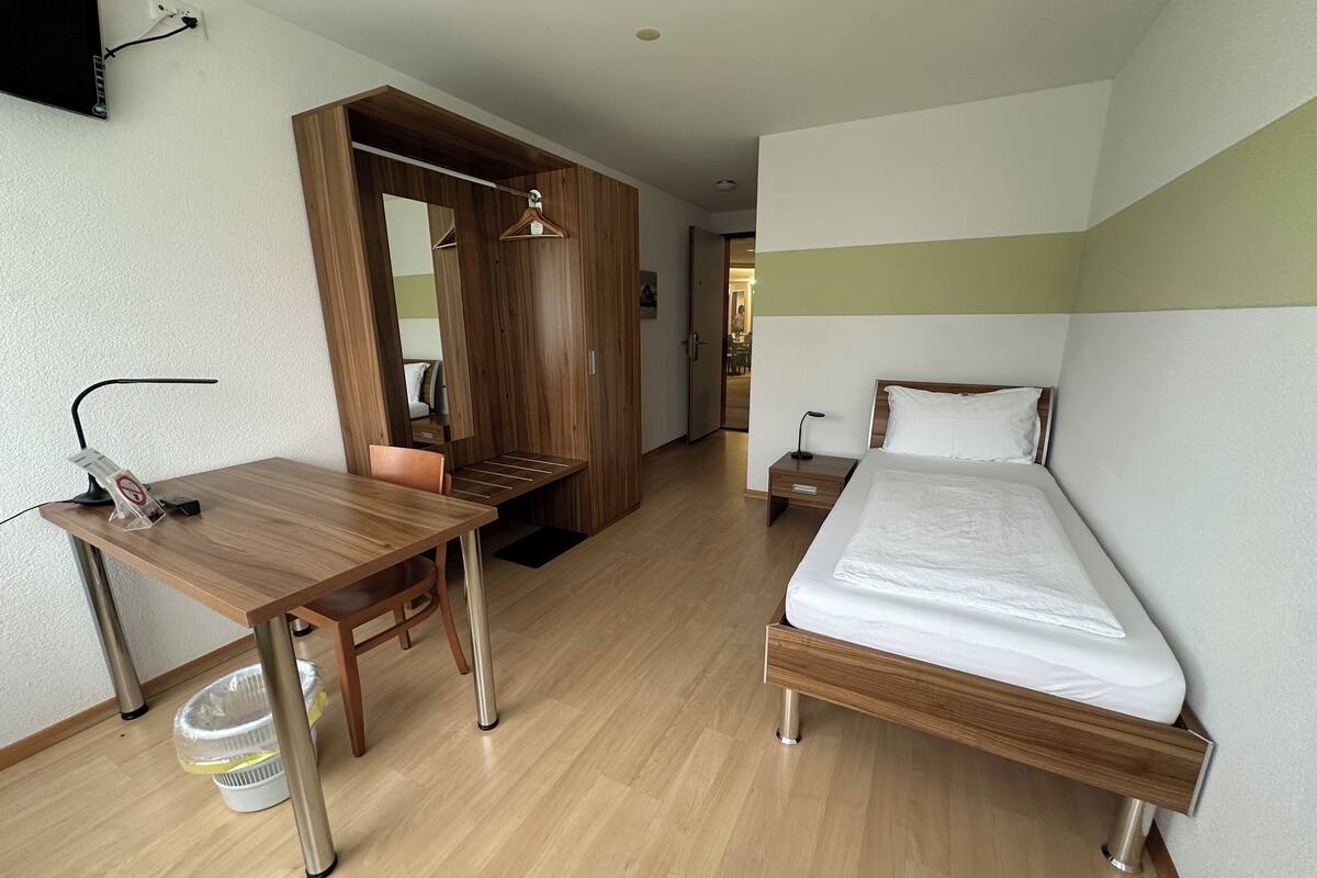 A hotel room with a wooden desk, a bed, a mirror, and a wardrobe.
