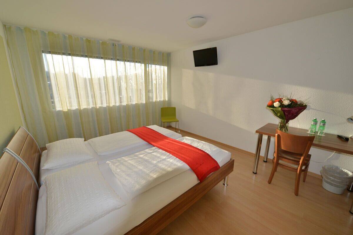 A hotel room with a large bed, a desk with a chair, a television, and a window with curtains.