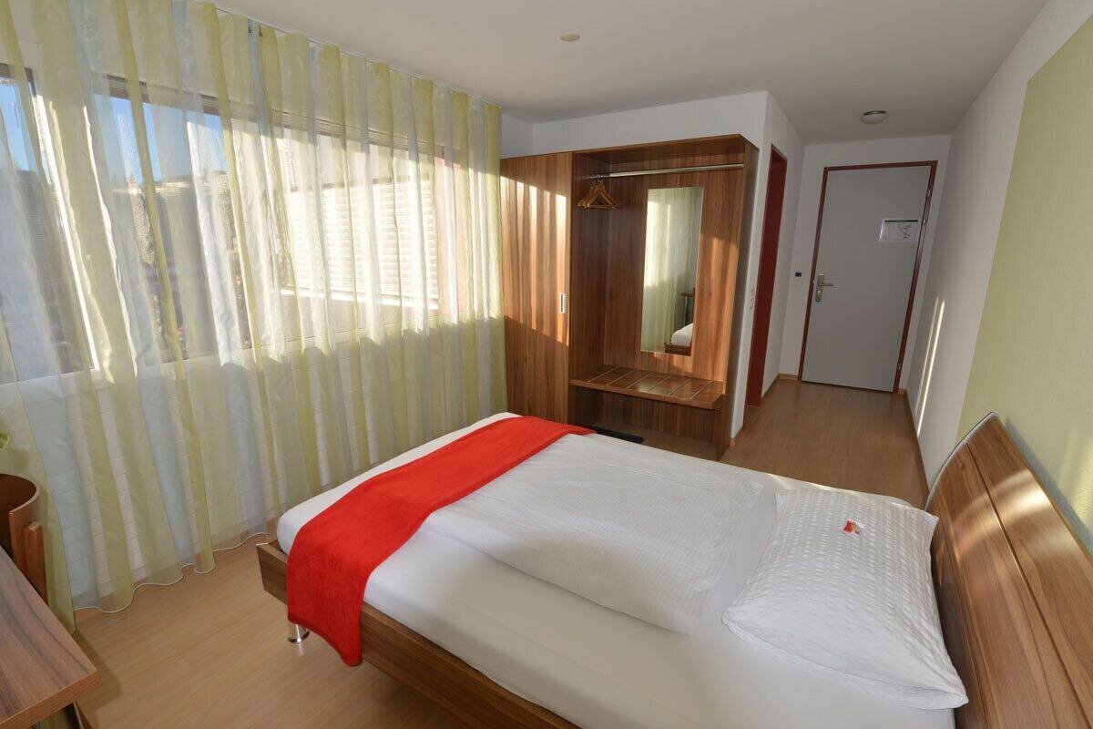 A hotel room with a bed, a wooden wardrobe, a mirror, and a door.