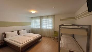 A room with a bunk bed, a double bed, a chair, and a window with curtains.
