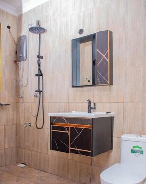 Un baño con ducha, lavabo con espejo e inodoro.