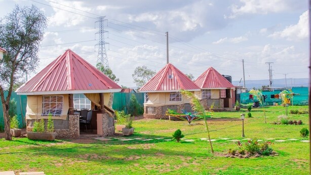 A residential area with two houses featuring red roofs and beige walls, surrounded by a well-maintained lawn and a paved walkway. - Enkapune Cowboy park resort (Kajiado)