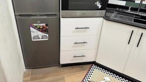 Une cuisine équipée d’un réfrigérateur en acier inoxydable, d’un four encastré et de meubles de rangement blancs.