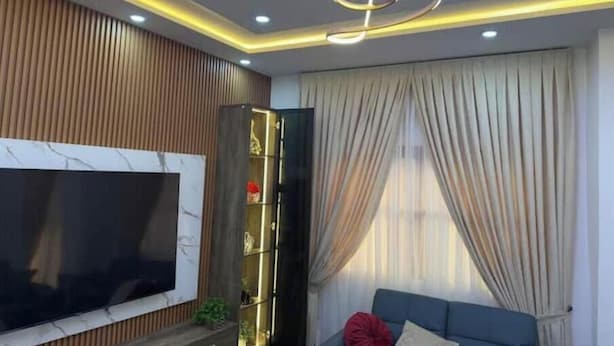 A modern living room with a flat-screen TV, a blue sofa, and a decorative ceiling light fixture.