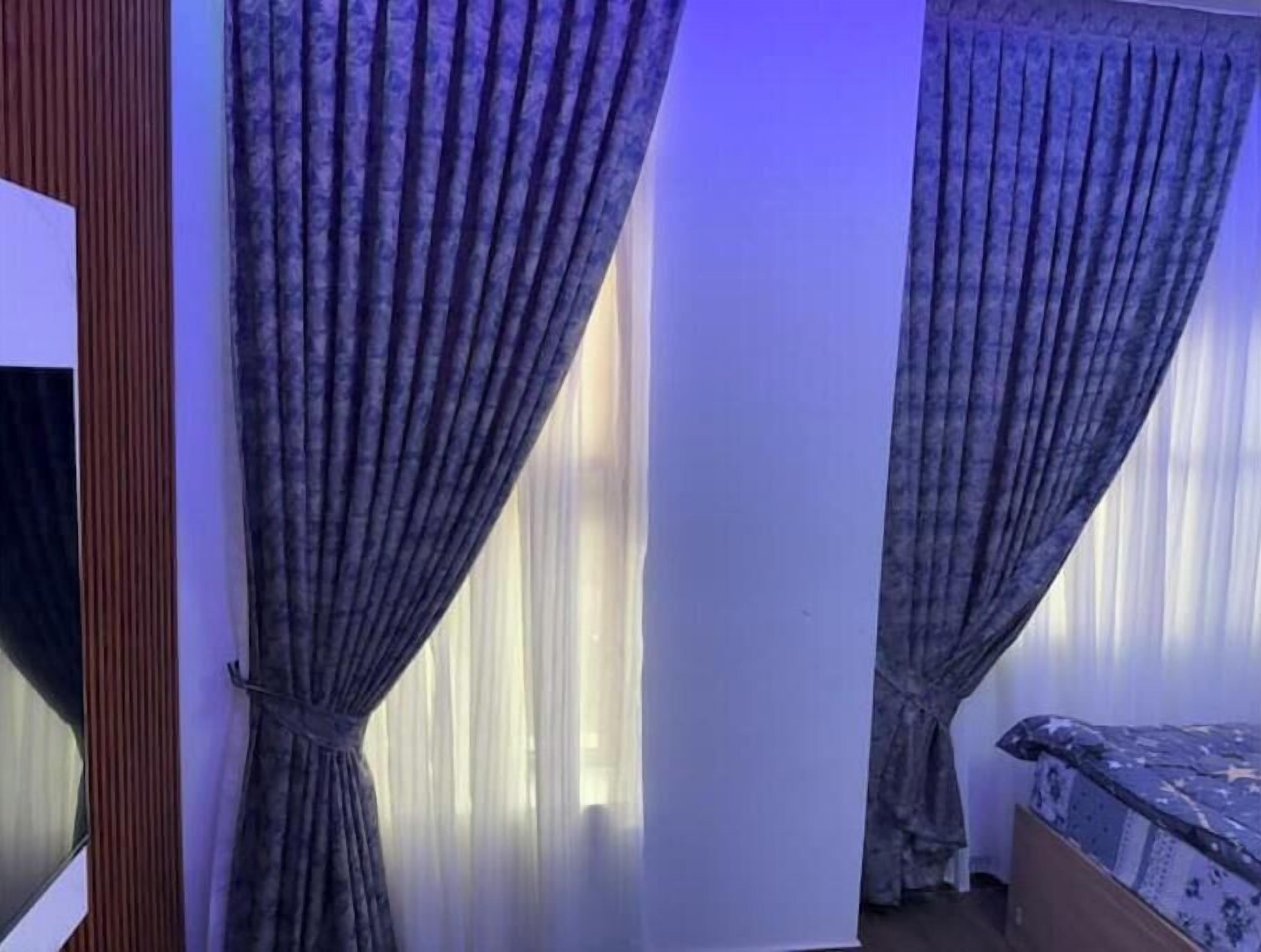 A room with a bed, a wooden wardrobe, and curtains.