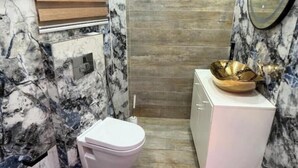 A compact bathroom with a marble backsplash, a white toilet, and a sink with a gold bowl.