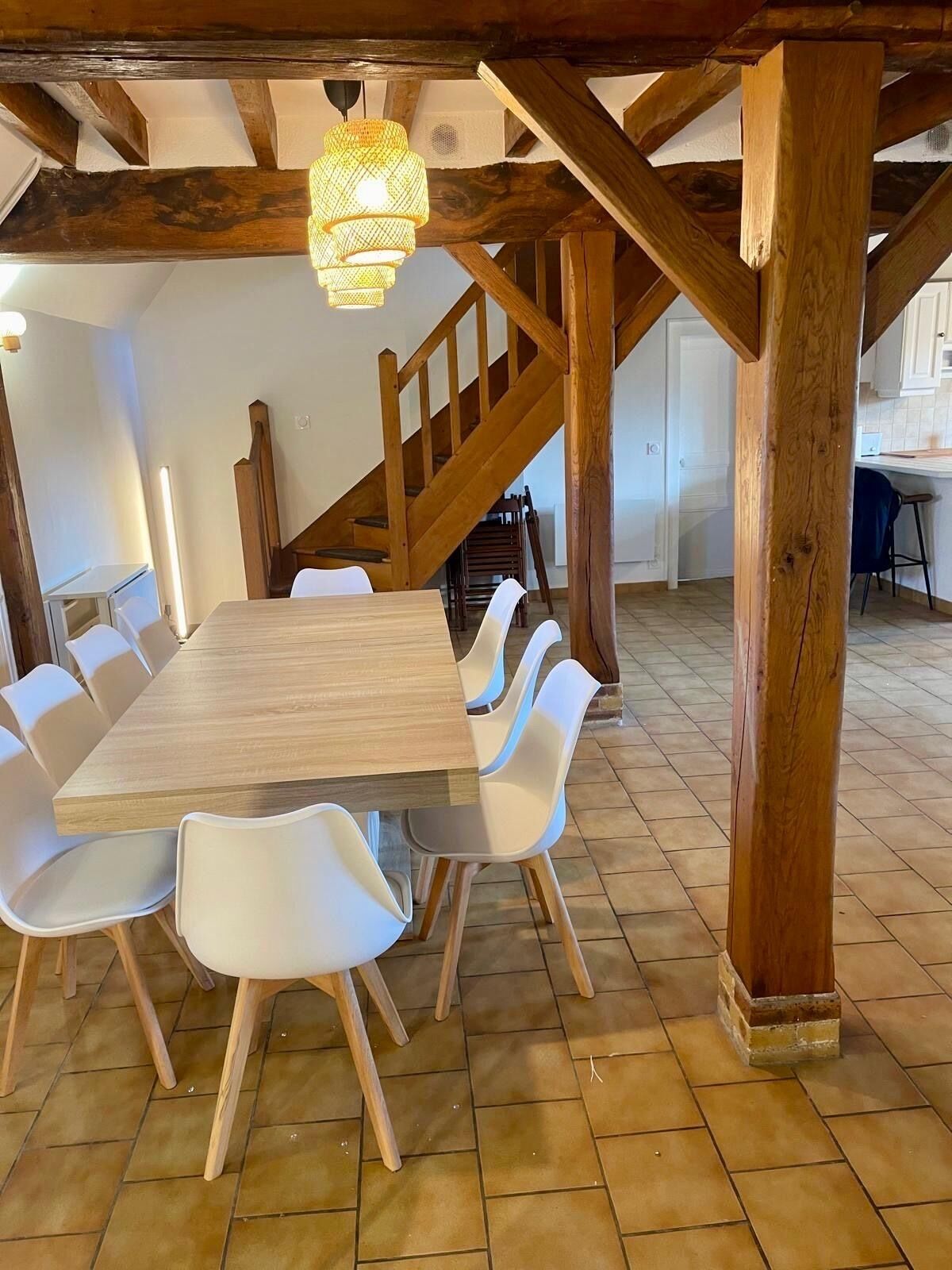 Ein Essbereich mit Holztisch und weißen Stühlen, eine Holztreppe und eine hängende Leuchte.