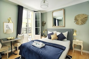 Habitación de hotel con cama, escritorio, silla, espejo y balcón.