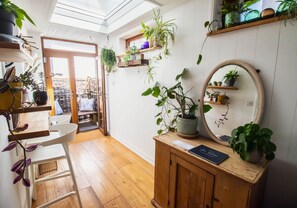 Ein Zimmer mit Holzboden, einem weißen Stuhl, einem Holzschrank mit Spiegel und verschiedenen Blumentöpfen.