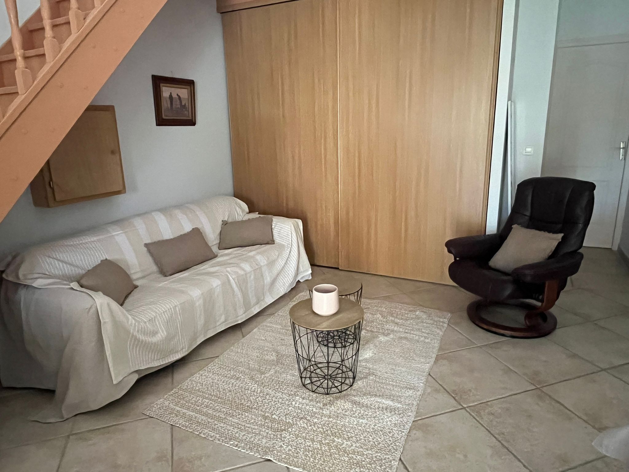 A living room with a sofa, a coffee table, a chair, a wooden door, and a staircase.