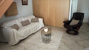 Un salon avec un canapé, une table basse, un fauteuil, une porte en bois et un escalier.
