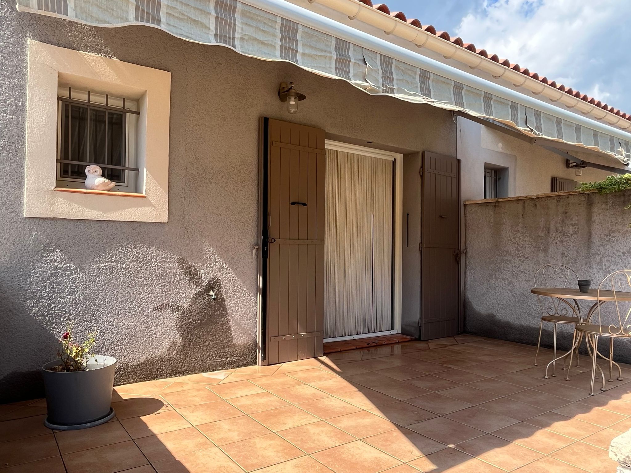 A building with a tiled patio, a door, a window with a bird figurine, and a potted plant.