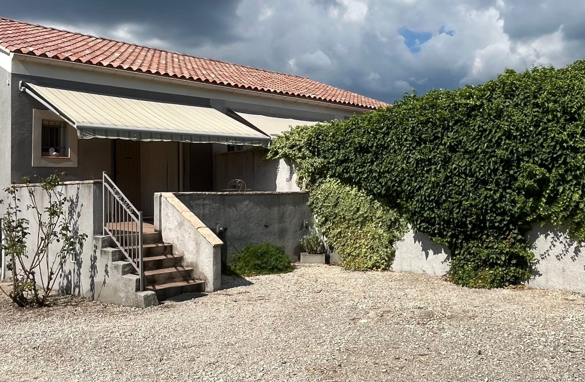 Une maison avec un toit recouvert de tuiles rouges, une véranda et une allée gravillonnée.