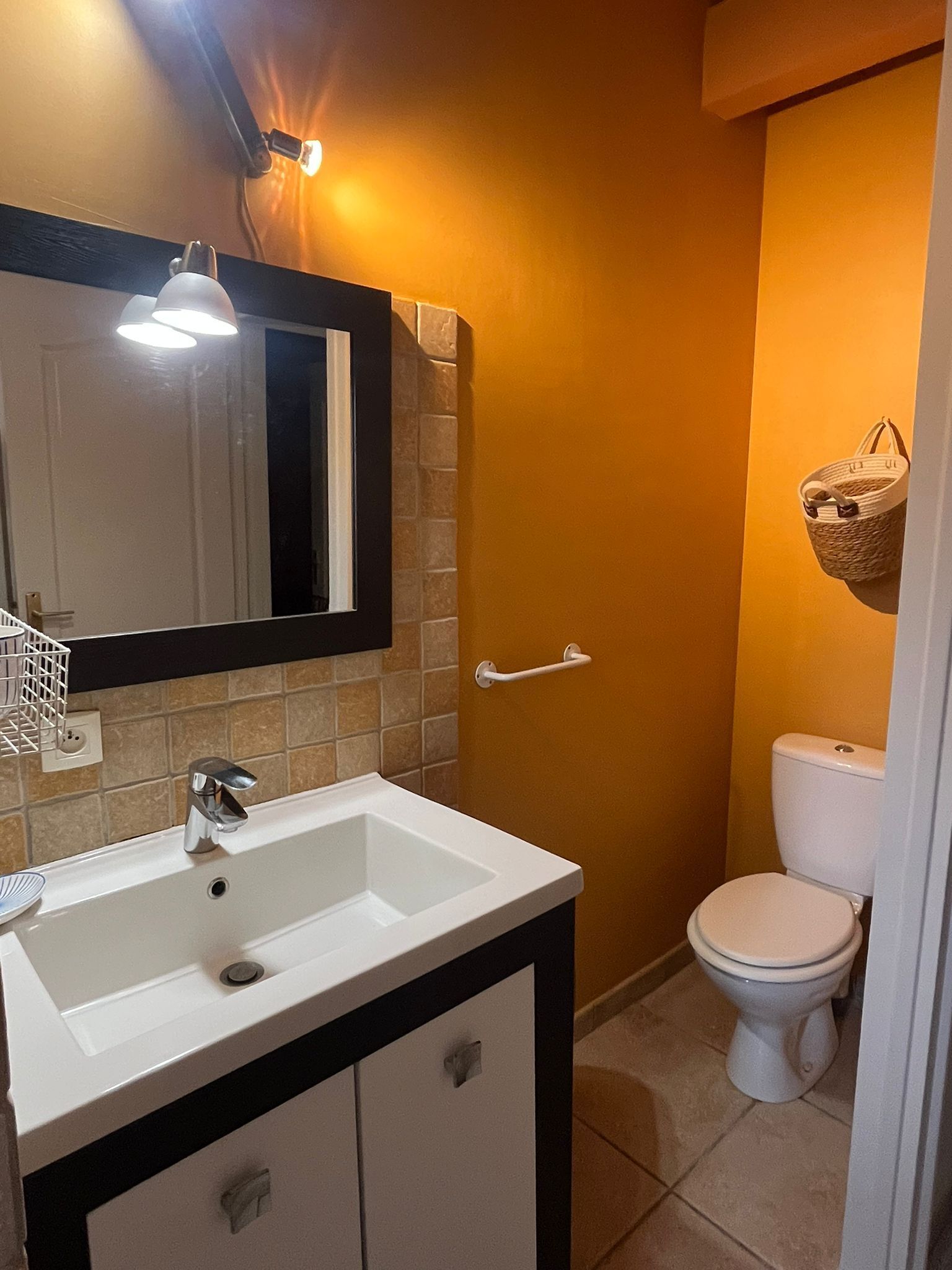Un baño con lavamanos blanco, un espejo, toallero y un inodoro.