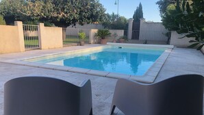 Une piscine dotée d’une terrasse carrelée, entourée d’un petit muret et agrémentée de plantes en pot.
