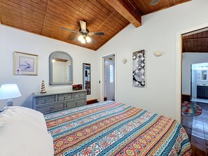Un dormitorio con cama, cómoda, ventilador de techo y obras de arte en las paredes.