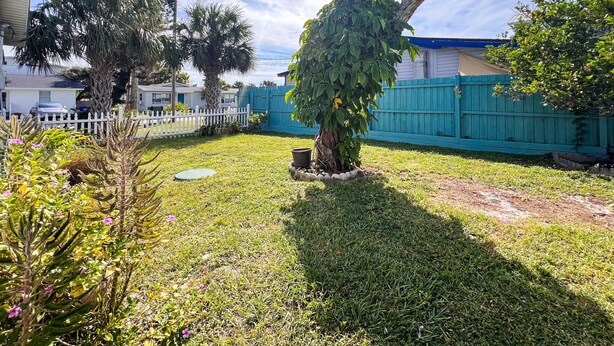 A backyard with a small tree, a white fence, and a blue fence. - Cottage & Bungalow | Coastal 2-Unit Retreat (St. Augustine)