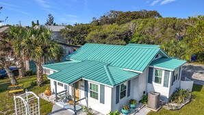 A single-story house with a green metal roof, a front porch, and a small garden area. - Cottage & Bungalow | Coastal 2-Unit Retreat (St. Augustine)