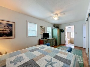 Un dormitorio con cama, televisor, ventilador de techo y puerta que da a otra habitación.