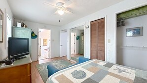 A bedroom with a bed, a television, a ceiling fan, and a wardrobe.