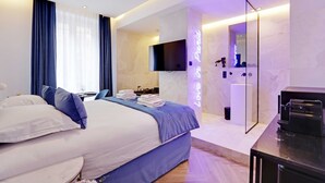 A modern hotel room with a large bed, a flat-screen TV, a mirror, and a bathroom with a shower and toilet.