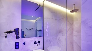 A modern bathroom with a marble wall, a large mirror, a sink, and a shower.