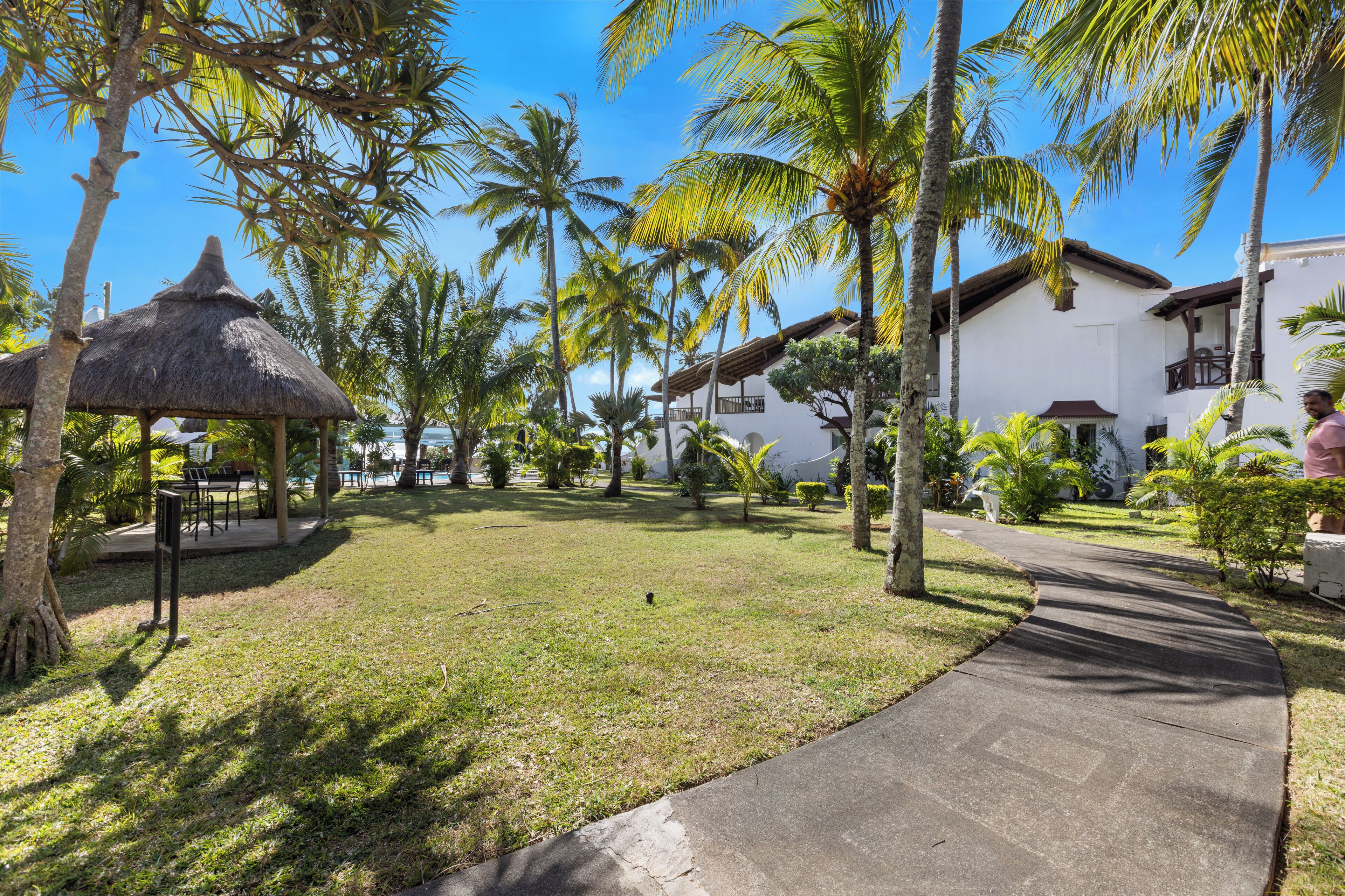 Ein Resort mit einem strohgedeckten Gazebo, Palmen und einem gepflasterten Weg.
