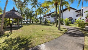 A resort with a thatched gazebo, palm trees, and a paved walkway.