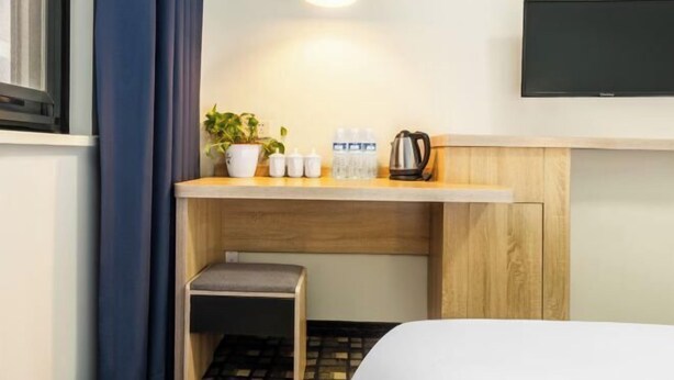 Ein Hotelzimmer mit Bett, einer kleinen Sitzecke, einer Küchenzeile mit Kaffeemaschine, einem Fernseher und einem fenster mit Vorhängen.