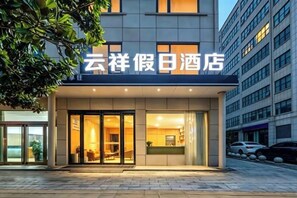 A hotel entrance with a sign, glass doors, and a paved walkway.