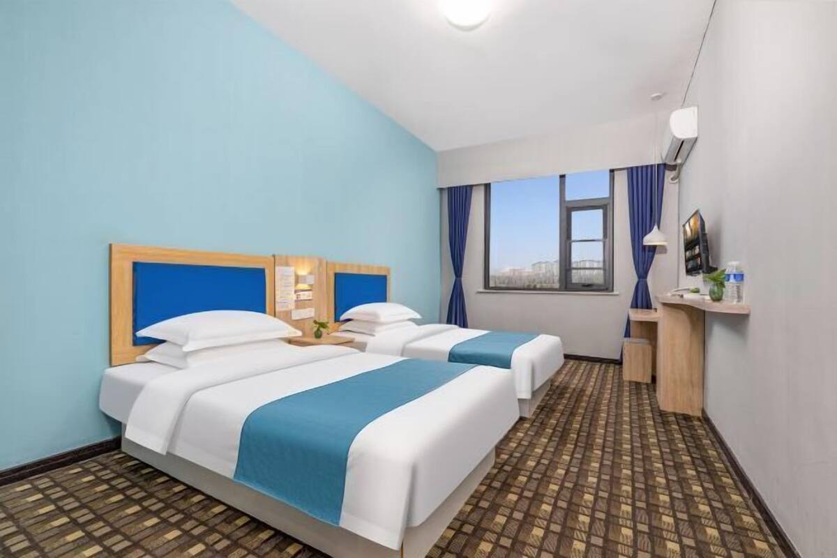 Ein Hotelzimmer mit zwei Betten, einem Schreibtisch, einem Fenster mit Vorhängen und einem gemusterten Boden.