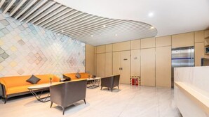 A modern hotel lobby with a curved ceiling, a seating area with a sofa and chairs, and a reception desk. - Yun xiang Holiday Hotel (Zhengzhou Xinzheng International Airport) (Xinzheng)