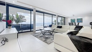 A modern living room with a white sofa, a coffee table, and a view of the ocean through large windows. - Villa Zenha in Ribeira Brava (Ribeira Brava)