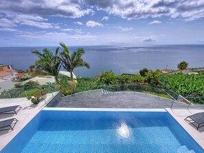 Una piscina con vistas al mar, rodeada de follaje y palmeras.