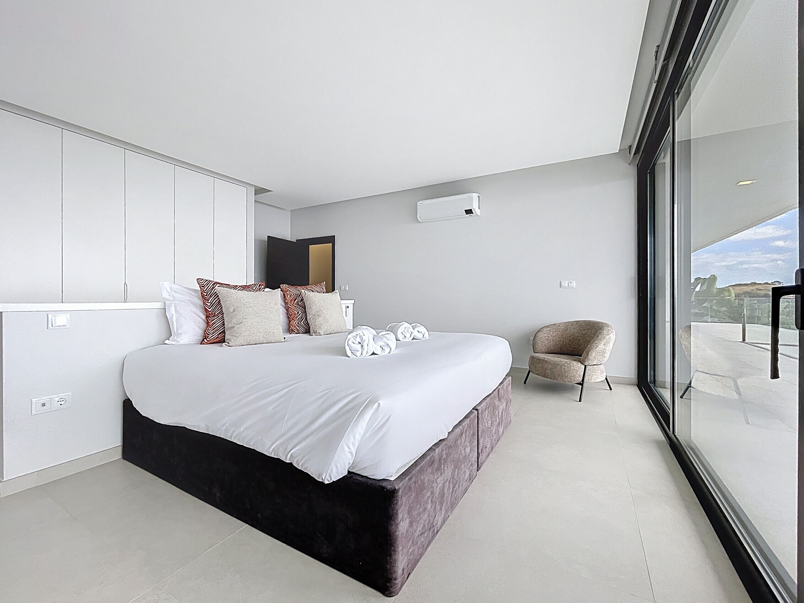 Un dormitorio moderno con una cama grande, una silla y vistas por un ventanal amplio.