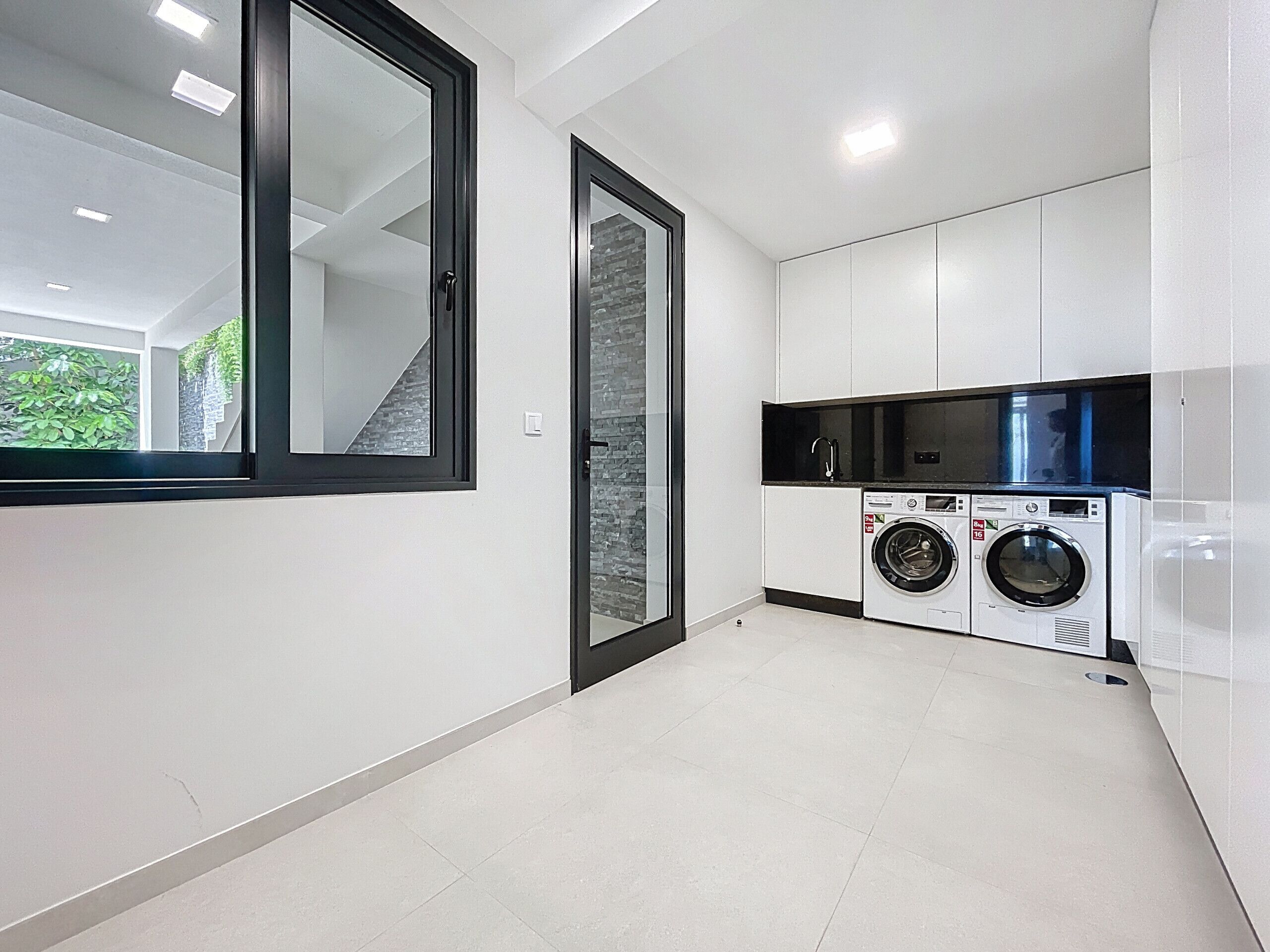 A modern kitchen with a built-in washer and dryer, white cabinetry, and a large window.