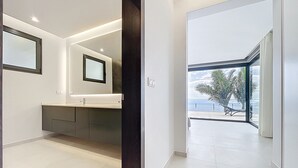A modern bathroom with a large mirror, a vanity with a sink, and a view of the outdoors through a glass door. - Villa Zenha in Ribeira Brava (Ribeira Brava)