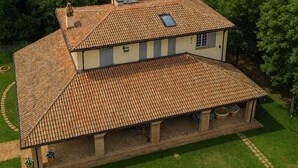 Una casa de dos pisos con techo de tejas, rodeada de colinas verdes y un cielo despejado.