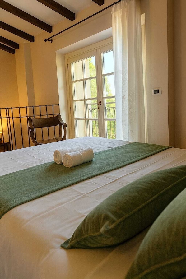 A hotel room with a bed, a window with curtains, a chair, and a view of greenery outside. - Tenuta Monte Bago (Medesano)
