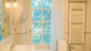 Un baño con dos lavamanos, inodoro, ducha con puerta de cristal y ventana con vistas a árboles.