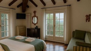 Un dormitorio con una cama grande, un sillón verde, suelo de madera y un televisor en la pared.