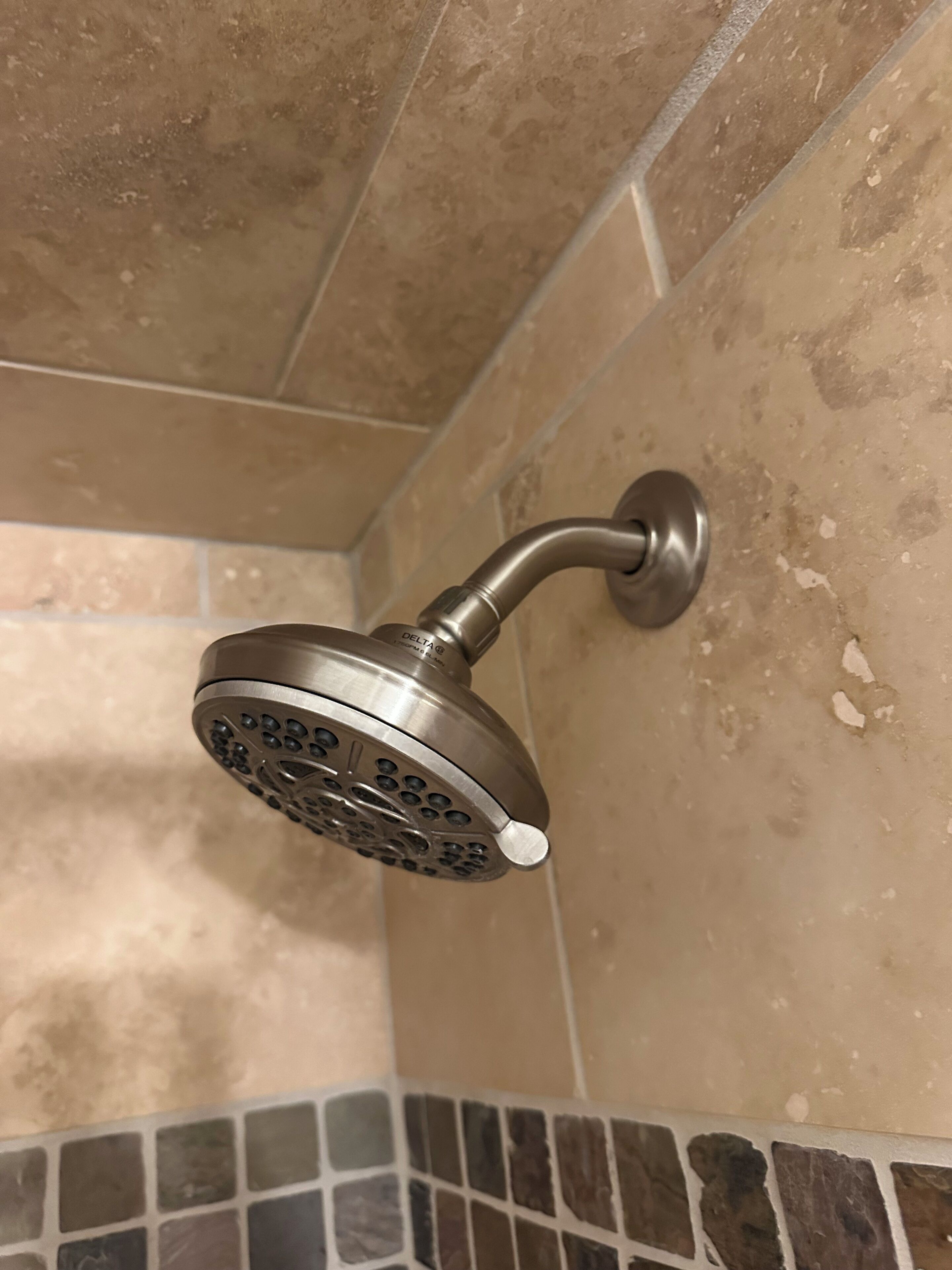 A showerhead with a curved design, mounted on a wall with beige tiles.