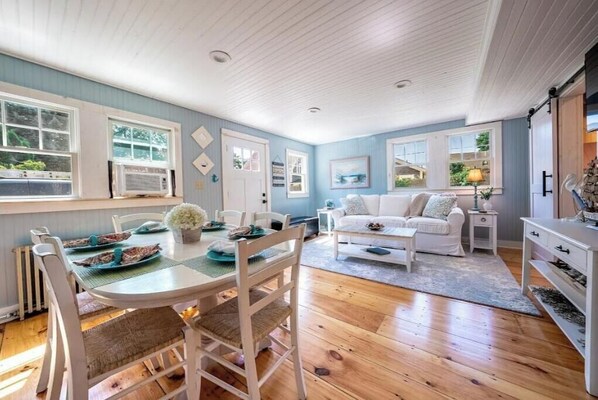 Una sala de estar acogedora con comedor, que presenta piso de madera, muebles blancos y una pared azul de acento.