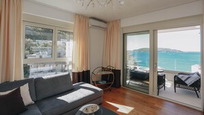 Een moderne woonkamer met een grijze bank, een klein rond tafeltje en uitzicht op zee door grote schuifdeuren.