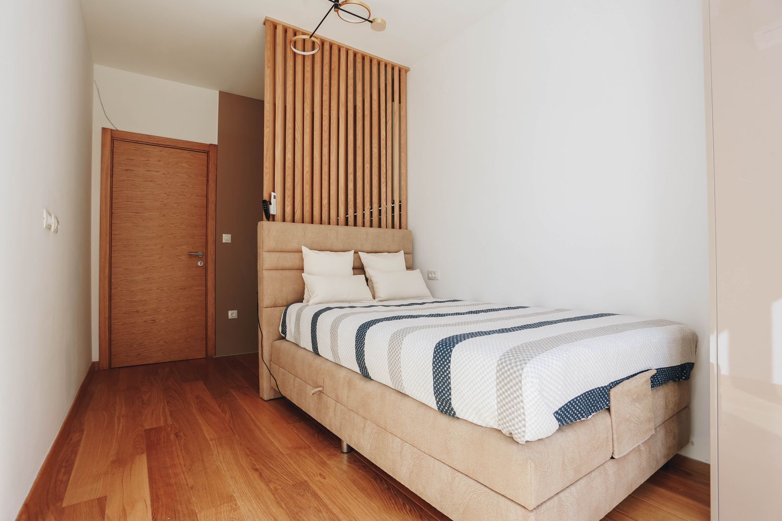 A bedroom with a bed, wooden slat headboard, and a wooden door.